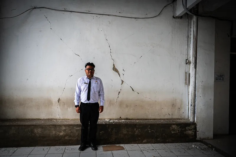 Ary Pelut standing beside a cracked wall inside the earthquake-damaged RSUD Ruteng hospital, Flores, Indonesia